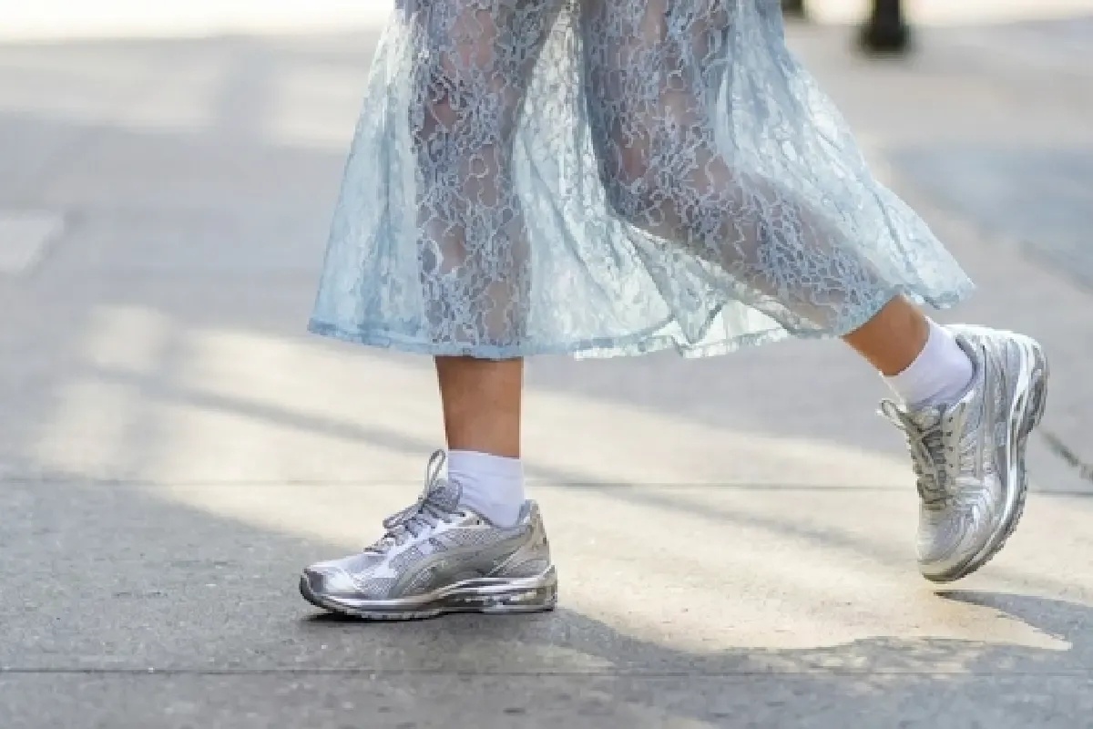 Woman wearing silver metallic technical sneakers styled with an icy blue lace skirt and grey blazer, illustrating the 2026 Wrong Shoe Theory, Cool Blue, and Maxi Lace fashion trends.