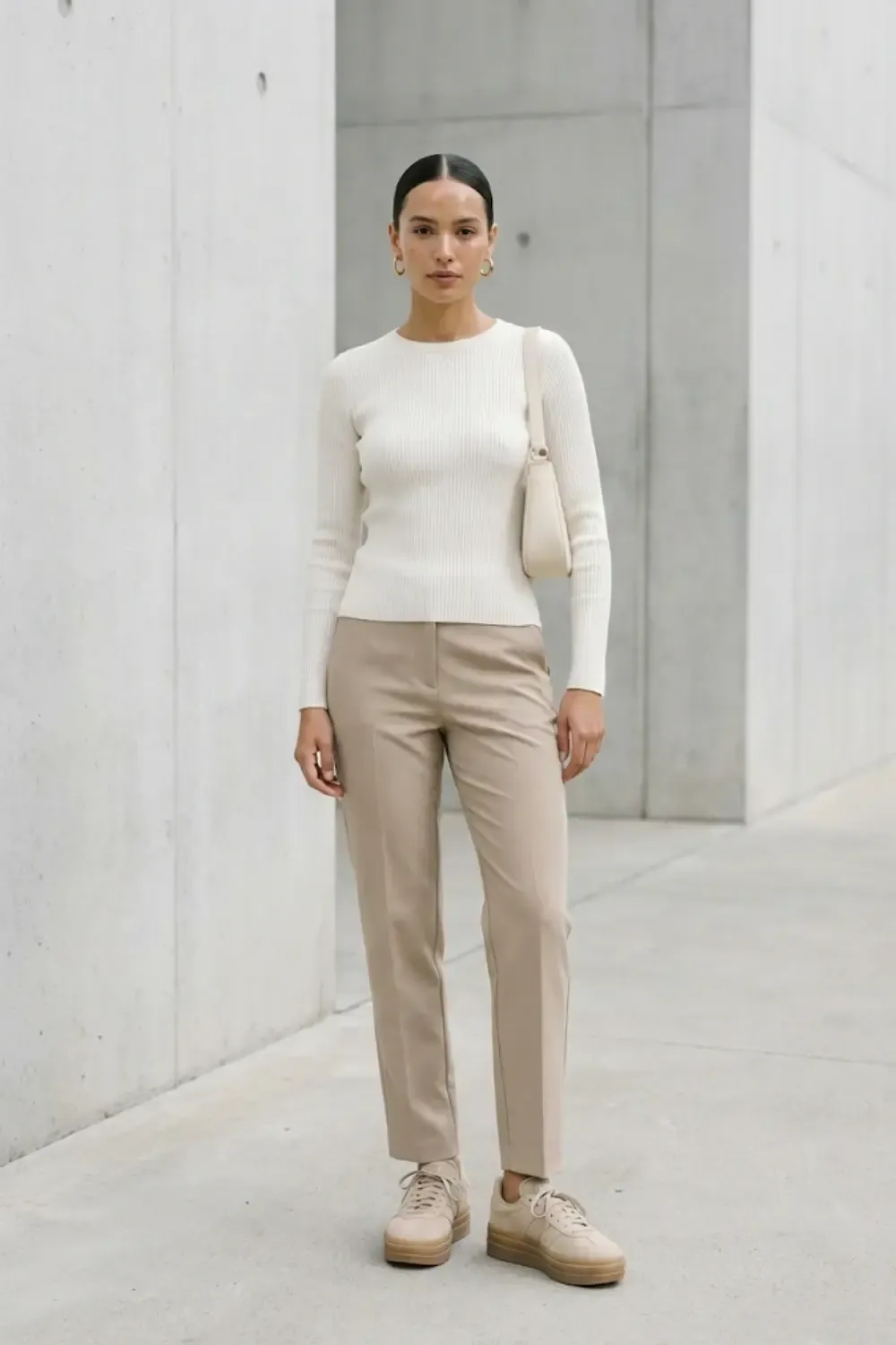 A model standing against a concrete wall wearing a minimalist outfit. She is wearing beige/sand-colored Adidas Gazelle Bold sneakers.